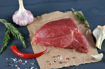 Wall Mural - Beef raw on kraft paper. Next to the meat are spices, garlic, rosemary, red hot chilli pepper. Close-up. View from above. Dark background.  Macro photography.