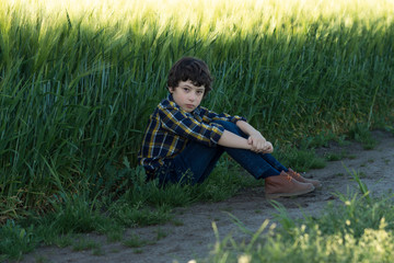 A sad boy in jeans and a shirt is sitting in the field.