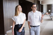 © Mangostar - Smiling male executive showing office to female colleague. Young Caucasian businessman wearing glasses walking with female partner and talking in office building. Meeting, employment concept