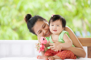 Wall Mural - Cute asian baby girl in Thai traditon dress smiling and playing with her mother and turtle doll with love and happiness