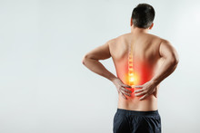 Rear View, The Man Holds His Hands Behind His Back, Pain In The Back, Pain In The Spine, Highlighted In Red. Light Background. The Concept Of Medicine, Massage, Physiotherapy, Health.