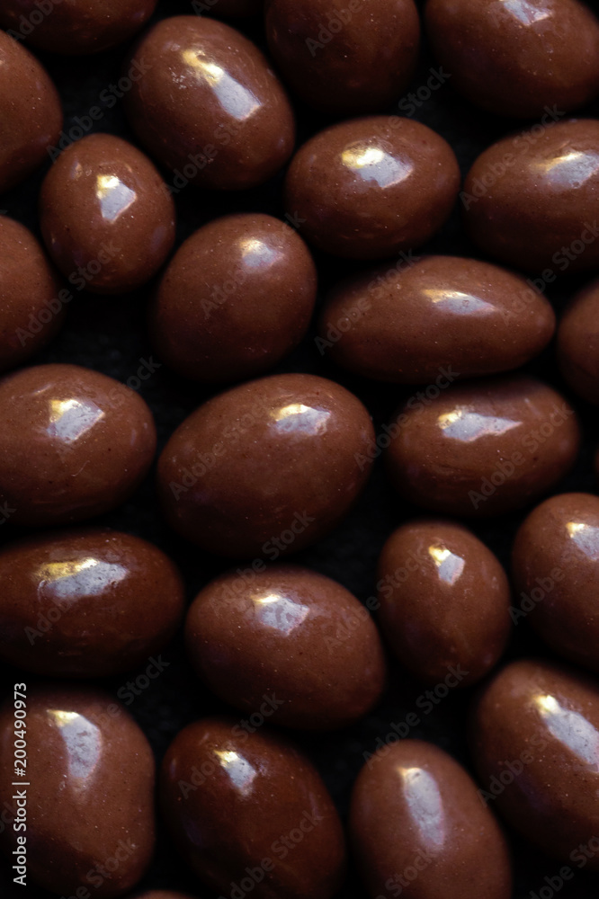 Chocolate candy textured background. Dark brown chocolate round candies on black concrete background top view close up. Adobe Stock