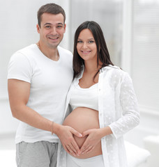 Wall Mural - husband and pregnant wife with folded hands in the shape of a heart on his tummy