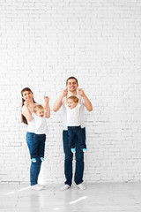 Happy young family with twins having fun playing on a white brick wall background, hugging each other and smiling