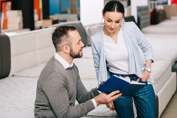 couple with notebook in furniture store with arranged mattresses