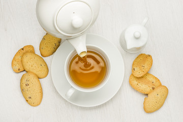 Poster - pouring tea into cup on white table with cookies and milk jug