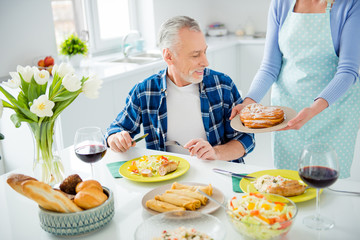 Sticker - Handsome man with bristle sitting at the table eating food having glass of red wine, woman holding in hands plate demonstrate tasty sweet baked bun to her lover, lovely couple enjoying dinner indoor