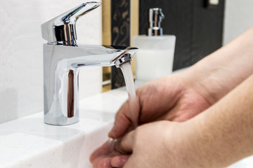 Wall Mural - water faucet in the bathroom or toilet. water flows from the tap into male hands. Hands blurred