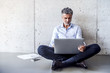 © Westend61 - Mature businessman sitting on the floor using laptop