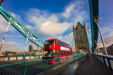 Wall Mural - London, England - Iconic red double-decker bus in motion on famous Tower Bridge with skyscraper of Bank District at background. Blue sky and clouds