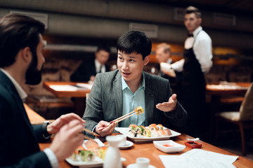 meeting with chinese businessmen in restaurant. two men are eating sushi.