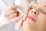 Powiększanie ust. Kosmetyczka ostrzykuje  twarz kobiety podczas zabiegu odmładzającego w klinice piękności.