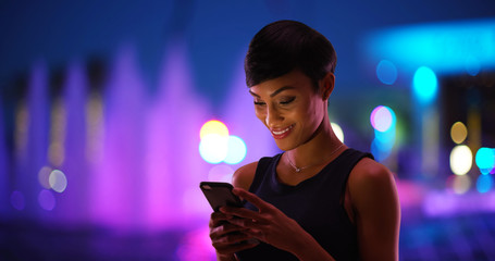 Wall Mural - Smiling young black woman texting on cell phone colorful fountain in background