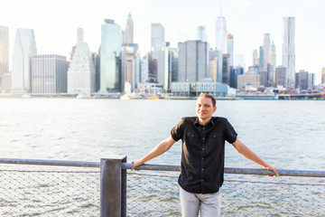 Wall Mural - Young man outside outdoors in NYC New York City Brooklyn Bridge Park by east river, railing, looking at view of cityscape skyline travel