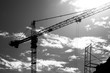 Black and white photo of a silhouette of a construction crane and bright sun with clouds