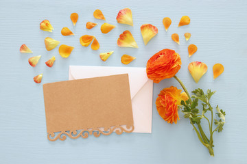 Image of envelope with delicate pastel orange and yellow beautiful flowers arrangement over blue wooden background. Flat lay, top view.