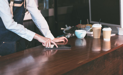 Poster - close up  barista waitress wear jean apron using tablet on counter bar to check stock in coffee shop.food and drink business.technology lifestyle.