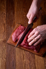 Wall Mural - Strong professional man's hands cutting raw beefsteak, selective focus, close-up