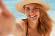 © WHstudio Leushin N - Attractive young woman with broad smile, healthy skin, rests on seashore, takes photo of herself, being in good mood, enjoys leisure and summer vacation. Beautiful female makes selfie against ocean