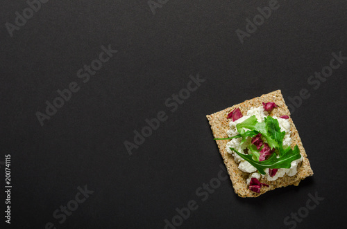 Fotografía Crisp bread with soft cream cheese and herbs on black background
