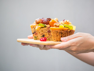 Female hand  holding a loaf of fruit cake on wooden plate