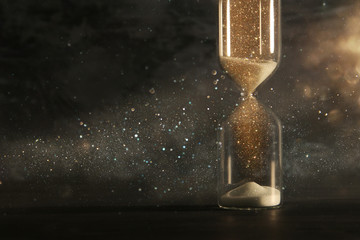 Wall Mural - Image of hourglass as time passing concept over black background for business deadline. Glitter overlay.