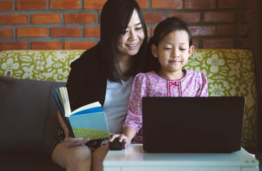 Asian daughter and mother using computer laptop at home with smile and happy.