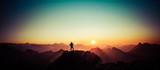 Fototapeta Sawanna - Man reaching summit enjoying freedom and looking towards mountains sunrise.
