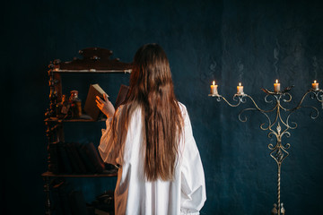 Wall Mural - Female puts old spellbook on shelf, back view