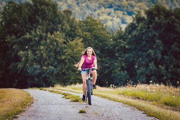 Wall Mural - Girl on bicycle cycling down a dirt path in summer, woods in the background