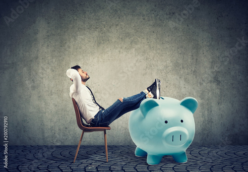 Cuadros en Lienzo businessman with big piggy bank relaxing sitting on chair