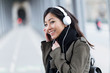 © nenetus - Smiling asian young woman listening to music and looking at camera in the street.