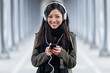 © nenetus - Smiling asian young woman listening to music and looking at camera in the street.