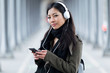 © nenetus - Pretty asian young woman listening to music and looking at camera in the street.