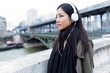 © nenetus - Pretty asian young woman listening to music and looking sideways in the street.