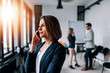 © bnenin - Portrait of a beautiful business woman talking on a phone in the office with collegues at the background.