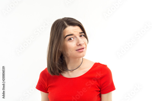 Portrait of a young brunette girl in red t-shirt looking suspiciously into the c Poster