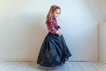 Sweet happy adorable fashion young little girl dressed like hipster hippie gipsy cowboy in sunglasses standing against white wall background in light bright room. Lifestyle people trendy concept