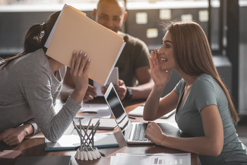 Aufkleber - Two satisfied women whispering while sitting together in boardroom. Colleague on background