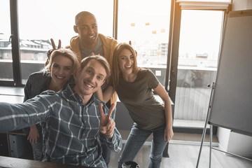 Aufkleber - Portrait of four happy people making snapshot of themselves at work. They are showing peace sign taking selfie in office