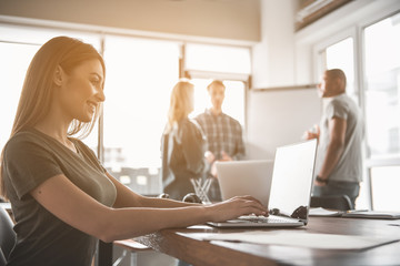 Aufkleber - Profile of smiling girl sitting and using computer. Her coworkers debating close to whiteboard on background