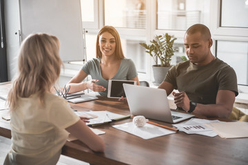 Wall Mural - Business people sitting at the wooden table. Girl pointing at tablet in her hand and smiling