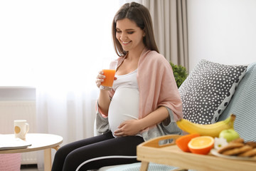 Wall Mural - Young pregnant woman holding glass with juice at home