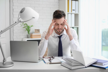 Poster - Man suffering from headache while sitting at table in office