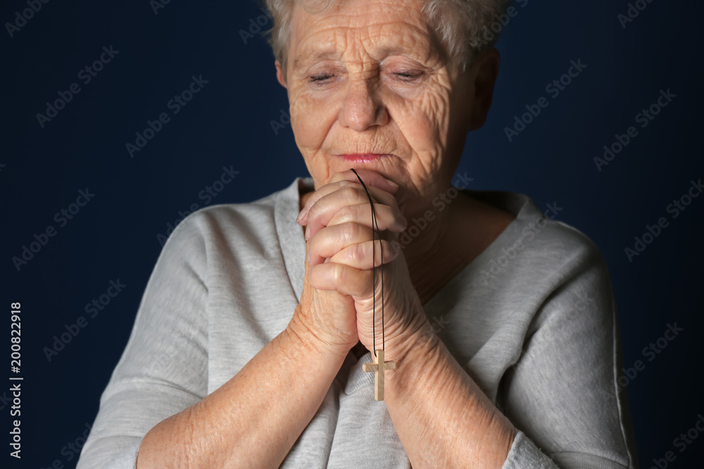 Religious elderly woman praying on dark background
