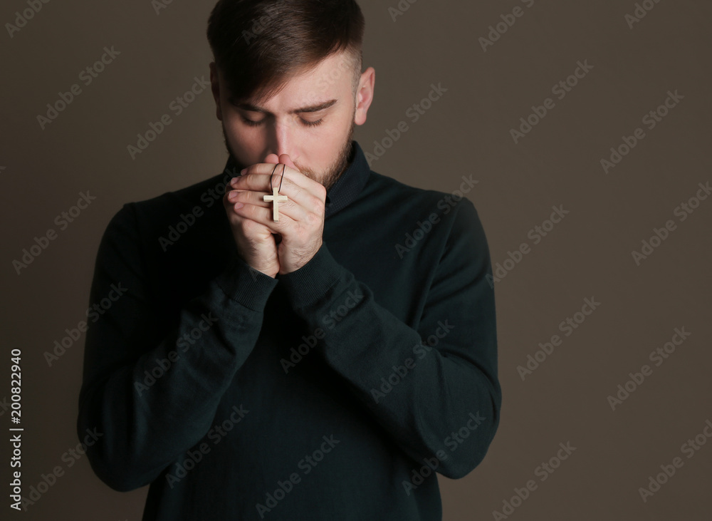Religious young man praying on dark background