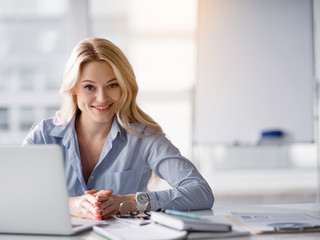 Poster - Waist up portrait of polite office worker listening to client attentively. She is looking forward and smiling. Woman is sitting at desk near laptop. Copy space