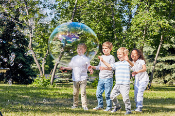 Wall Mural - multi-ethnic group of children having fun with big soap bubbles while spending warm summer day at pu