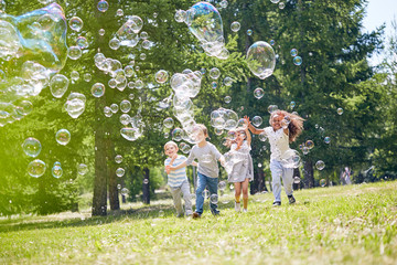 Wall Mural - group of cheerful little friends with wide smiles on their faces catching colorful soap bobbles whil