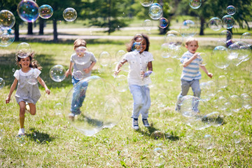 Wall Mural - cute little kids enjoying warm summer day outdoors: they running about green lawn of public park and